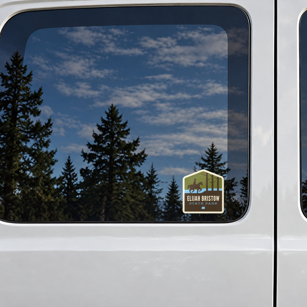 Elijah Bristow sticker on the rear window of a van, reflecting conifers and blue sky