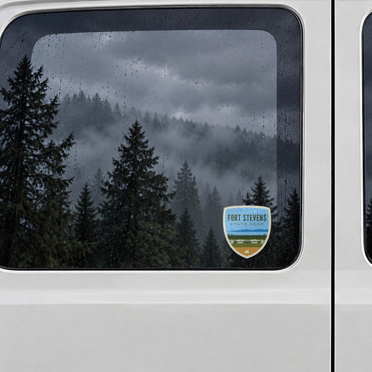 Fort Stevens Battery sticker on the rear window of a van, reflecting a misty forest in the rain