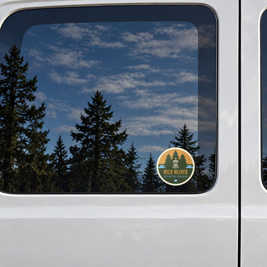 Milo McIver sticker on the rear window of a van, reflecting conifers and blue sky