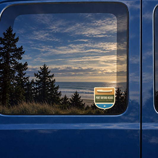 Port Orford Heads sticker on the rear window of a van, reflecting a beach at sunset