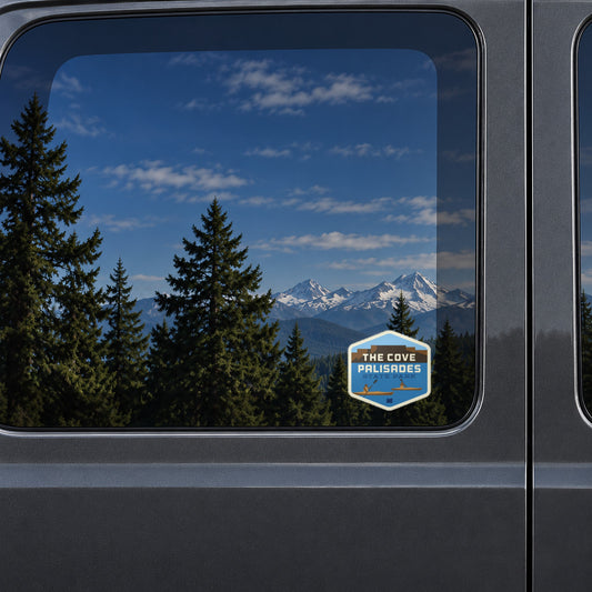 The Cove Palisades Kayaking sticker on the rear window of a van, reflecting snowy Cascade peaks