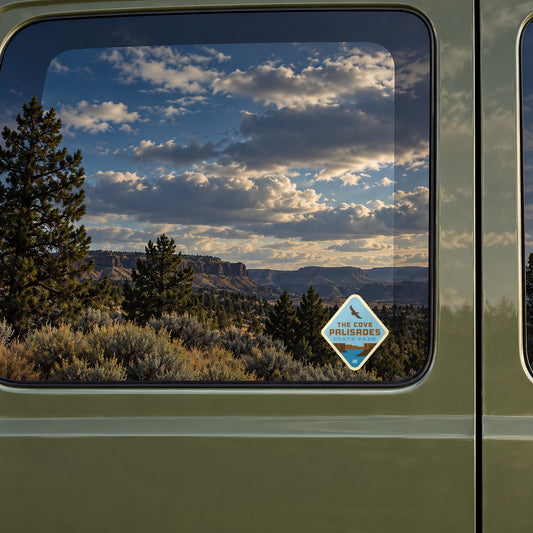 The Cove Palisades sticker on the rear window of a van, reflecting high-desert rimrock