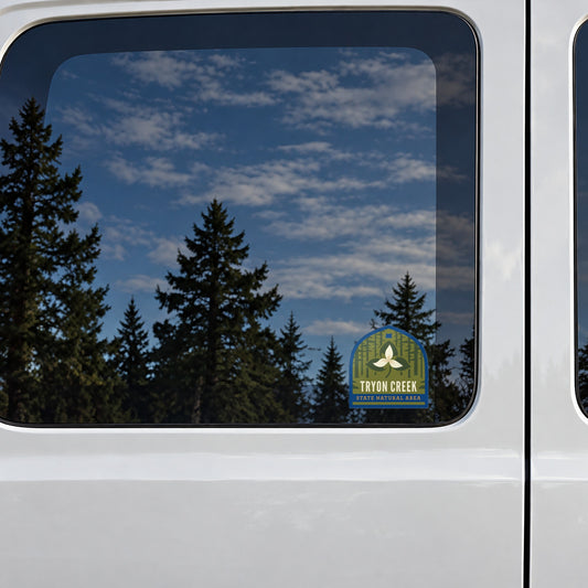 Tryon Creek sticker on the rear window of a van, reflecting conifers and blue sky