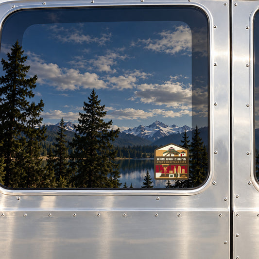 Kam Wah Chung sticker on the rear window of a van, reflecting a lake under snowy peaks
